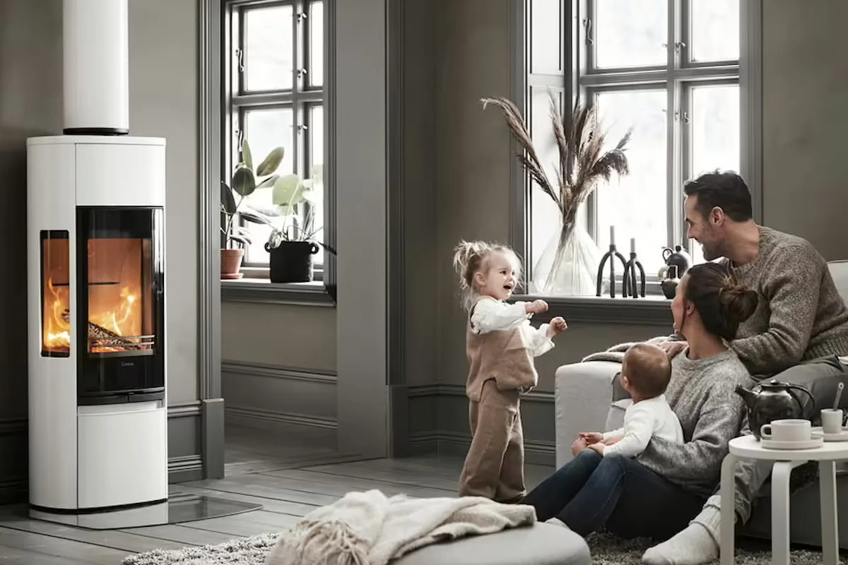 Hvit peisovn med flammer i en stue der en familie med to små barn sitter på gulvet